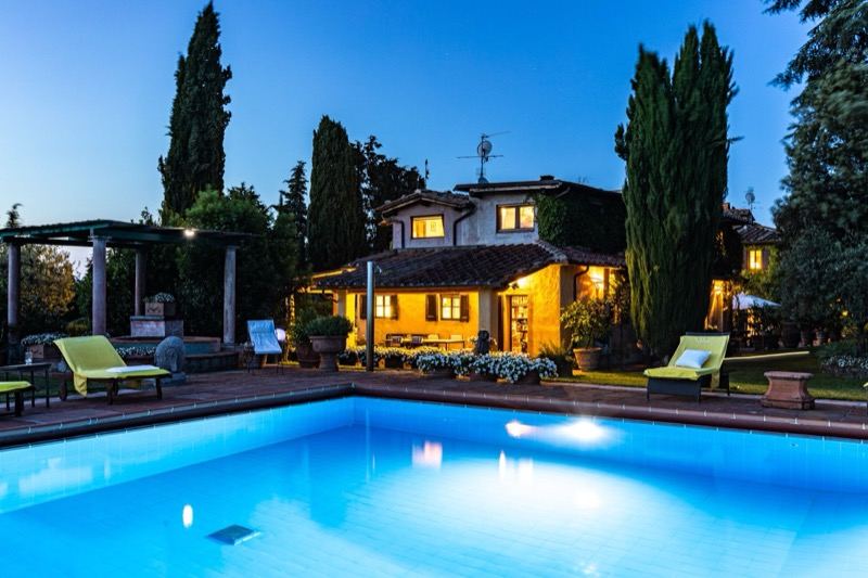 The pool lit at dusk with the pool house