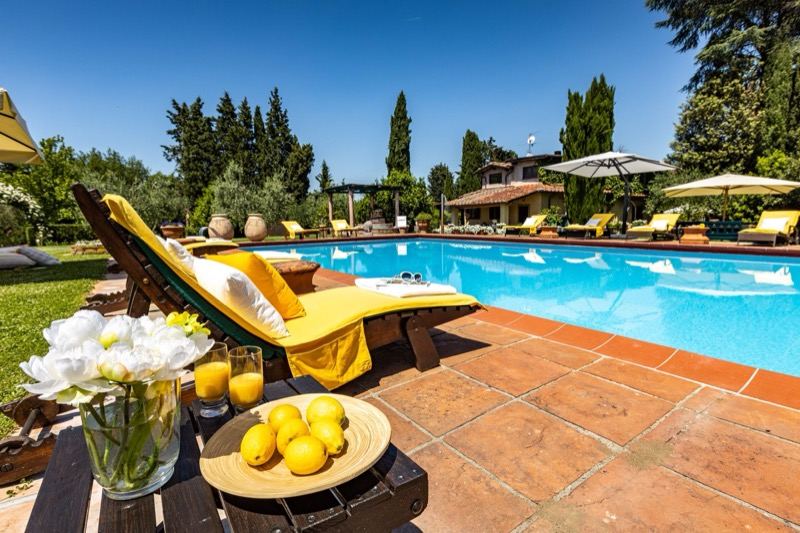 Sun lounger with yellow towel, flowers and lemons by the pool