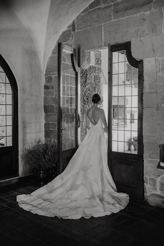 The bride from behind at the villa's stone door, in black and white